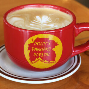 Red Latte Mug with Polly's Leaf logo surrounded by yellow circle. Latte mug is filled with a Latte
